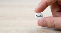 Hand holding white pill capsule labeled placebo on wooden surface for medical research and pharmaceutical testing concepts.