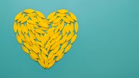 Yellow paper leaves arranged in a heart shape on a turquoise background with copy space for love and nature concepts.