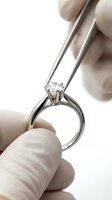 Jeweler holding diamond solitaire engagement ring with tweezers for inspection, close-up of white metal band and gemstone for jewelry retail and luxury branding.