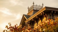Victorian mansion rooftop with ornate ironwork details glowing in warm golden sunset light, surrounded by vibrant autumn foliage.