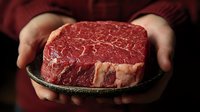 Raw beef ribeye steak held in hands against dark background, showcasing marbling and texture for premium cooking presentation.