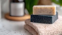 Natural handmade soap bars in beige and charcoal colors stacked on soft cotton spa and wellness concept.