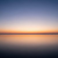 Serene sunset over calm water with gradient sky transitioning from deep blue to warm orange creating peaceful reflection for meditation and wellness content.