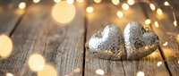 Silver heart-shaped Christmas ornaments on rustic wooden surface with warm golden bokeh lights creating festive holiday atmosphere for seasonal decorating.