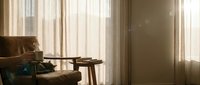 Cozy living room interior with leather armchair, wooden side table and warm sunlight streaming through sheer curtains creating peaceful atmosphere.
