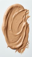 Creamy beige foundation or concealer swatch with textured brushstrokes and particles isolated on white background, suitable for cosmetics and beauty design projects.
