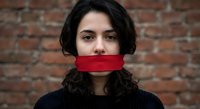 Young woman with dark curly hair wearing red face mask against brick wall background. Concept of health protection, pandemic safety measures.
