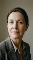 Mature woman with brown hair and fair complexion wearing olive blazer against neutral background, suitable for corporate portraits and professional headshots.