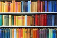 Colorful collection of vintage hardcover books arranged on wooden library shelves creating rainbow pattern, spines showing variety of sizes and colors.