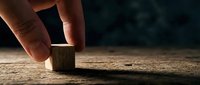 Hand placing wooden cube block on rustic surface with dramatic lighting for business strategy and building concepts.