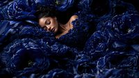 Young Asian woman surrounded by deep blue peonies in dramatic lighting, eyes closed in peaceful expression, artistic portrait capturing ethereal beauty and serenity.