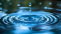 Mesmerizing water drop splash creating concentric ripples on blue water surface with floating droplets captured in high-speed macro photography.