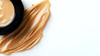 Creamy peanut butter spread and jar on white background, smooth texture with glossy swirls showing natural organic consistency and rich nutty appearance.