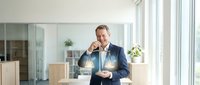 Middle-aged Caucasian businessman in navy suit holding glowing light bulb in modern office, representing innovation and creative business solutions.