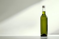 Green glass bottle with olive oil on white surface against light gray background with diagonal shadow, minimalist composition for food and beverage marketing.