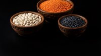 Assorted legumes in woven bowls on black background. White beans, red lentils, and black lentils displayed for cooking, nutrition, and food ingredient use.