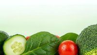 Fresh organic vegetables including broccoli, spinach leaves, cucumber slices and cherry tomatoes arranged on light background for healthy eating concepts.