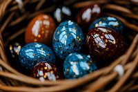 Decorative Easter eggs in blue and brown colors with gold speckles arranged in woven basket, close-up view showing glossy surface and artistic pattern.