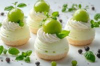 Gourmet individual desserts with creamy frosting, fresh green apples, mint leaves and chocolate pearls on white background. Perfect for bakery, pastry, food styling and culinary content.