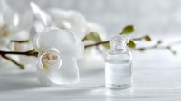 Elegant glass bottle with essential oil next to delicate white orchid flowers on light wooden surface, perfect for spa and wellness concepts.
