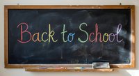 Colorful chalk text spelling Back to School written on dark classroom blackboard with wooden frame and chalk pieces for education concepts.