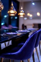 Elegant dining setup with blue velvet chairs and pendant lights creating atmospheric bokeh effect, modern restaurant interior with luxurious table settings.