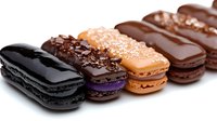 Colorful French macarons and eclairs arranged in row on white background. Assorted pastries with chocolate glaze and decorative toppings for bakery menu.