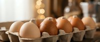 Fresh organic eggs in cardboard carton on rustic kitchen counter with warm bokeh lighting for cooking and baking recipes.
