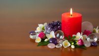 Red candle burning surrounded by healing crystals amethyst rose quartz and white flowers on wooden surface for meditation wellness spa relaxation therapy.