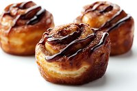 Fresh baked cream puffs with dark chocolate drizzle and caramelized sugar coating on white background, close up view of gourmet French pastry desserts.