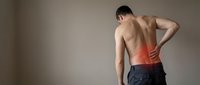 Young athletic Caucasian man experiencing lower back pain, holding spine area with red inflammation highlight, fitness injury concept for healthcare materials.