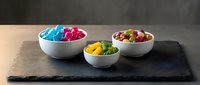 Colorful candy assortment in white ceramic bowls on dark slate board, sweet confectionery display for dessert presentation and food styling concepts.