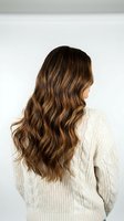 Young woman with long wavy brown hair wearing cream cable knit sweater viewed from behind against white background for hair care and fashion concepts.