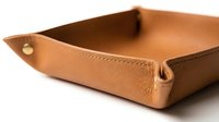 Tan leather valet tray with stitched edges and brass snap, elegant desk organizer for keys and accessories, isolated on white background.