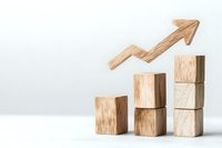 Wooden blocks arranged as ascending stairs with upward arrow showing growth trend on white background, business concept visualization for success.