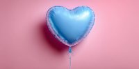Blue heart-shaped foil balloon floating against pastel pink background, creating romantic contrast for celebration or party decoration.