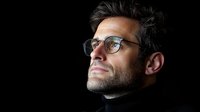 Dramatic side profile portrait of confident mature businessman wearing glasses against dark background, illuminated from above, showing determination.