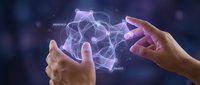 Hands reaching toward glowing neural network brain with connecting nodes and synapses on dark blue background representing artificial intelligence and machine learning.