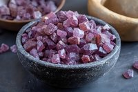 Pink Himalayan salt crystals in rustic stone bowl on dark background, raw mineral chunks with natural crystalline texture and varying shades of rose color.