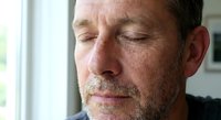Middle-aged Caucasian man with beard and mustache in contemplative moment by window with soft natural lighting for wellness and mindfulness concepts.