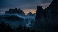 Dramatic mountain landscape with towering rock formations shrouded in mist at twilight, featuring a winding river through forested valley for nature and travel projects.