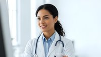 Professional female doctor with stethoscope smiling confidently in medical office wearing white coat for healthcare and medicine concepts.