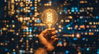 Hand holding glowing vintage Edison bulb against blurred city lights background at night. Innovation, creativity and bright ideas concept for business presentations.