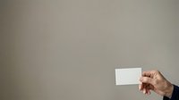 Hand holding blank white business card against neutral gray background, suitable for corporate branding, marketing mockups, and professional presentations.