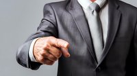 Businessman in gray suit pointing finger forward, demonstrating leadership and decision-making in professional corporate environment.