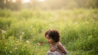 Woman with curly hair sitting in wildflower meadow during golden hour, enjoying nature and outdoor relaxation in sunny field setting.