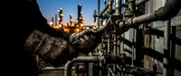 Industrial worker in protective gloves operating valve at oil refinery during sunset. Heavy industry, petroleum processing, safety equipment concept.