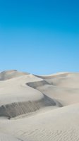 Vast desert landscape with undulating sand dunes featuring dramatic shadows and ripple patterns under clear blue sky, suitable for travel and nature backgrounds.