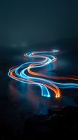 Long exposure light trails in vibrant neon blue and orange flowing across dark rocky terrain at night, creating dynamic glowing patterns for abstract and modern design projects.