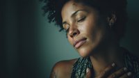 Young African American woman with natural curly hair in peaceful meditation pose against teal background, expressing serenity and mindfulness.